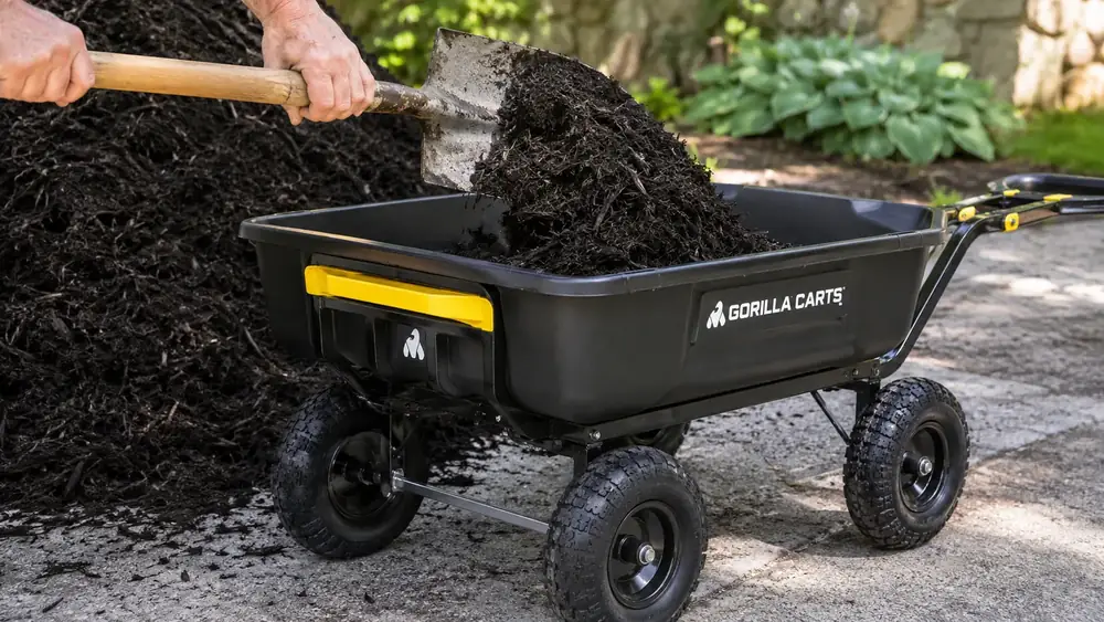 Hands loading mulch into a black poly dump cart tub positioned low and centered over the wheels